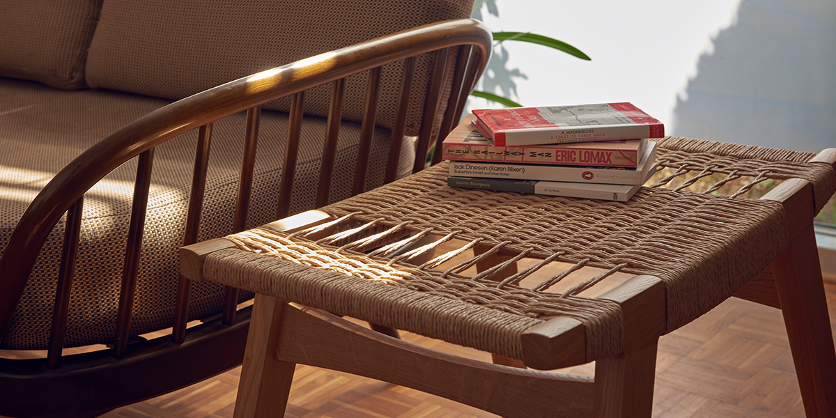 Photo of a natural oak and natural Danish Cord par-avion co. pi stool next to a sofa, a stack of books placed on the stool.