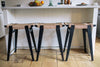A photo of 3 kitchen stools arranged at a kitchen island.  The stools are in the ebonised/black oak finish with natural Danish cord seats and the kitchen island behind is a painted white wood with various food items sitting on top.